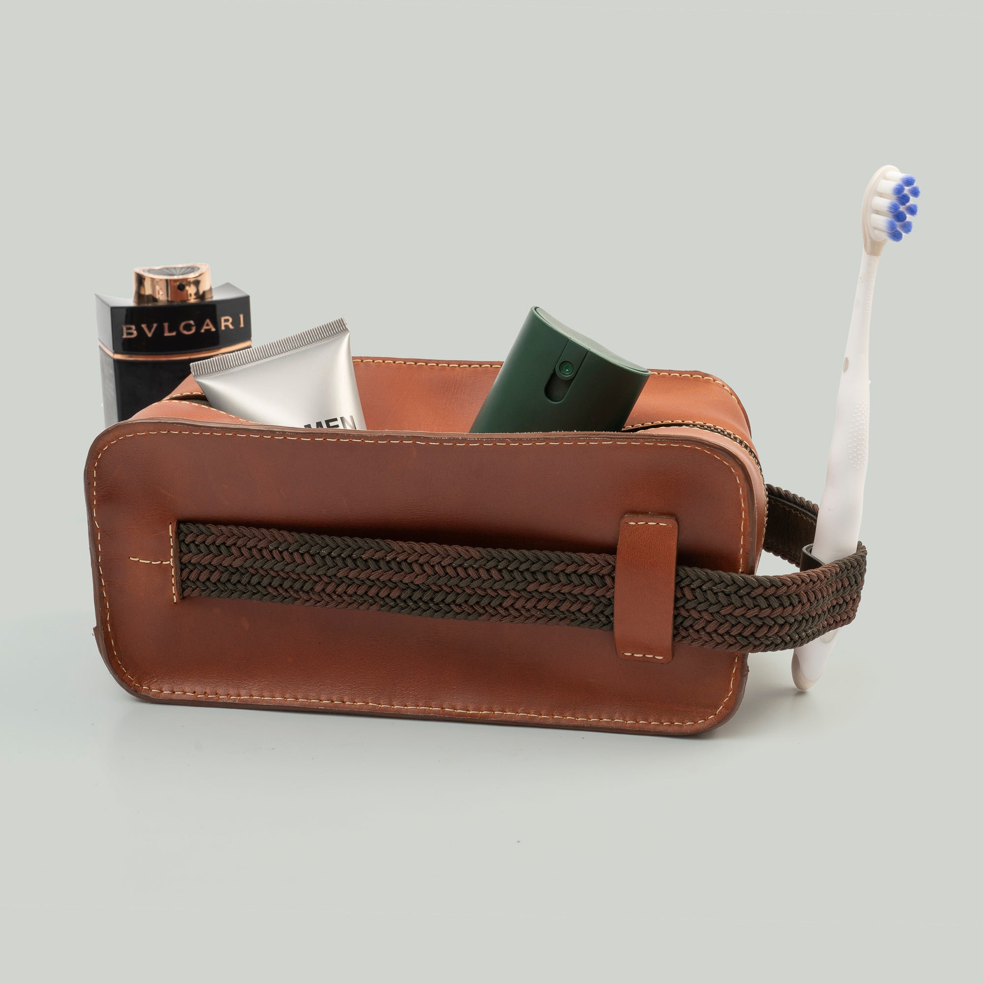 A brown leather travel pouch containing a toothbrush, toothpaste, and various toiletry items for personal care.